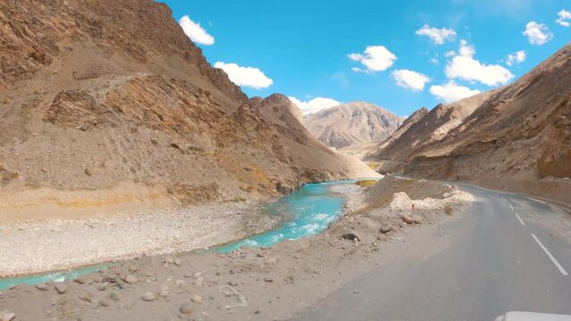 4K shot of blue coloured Zanskar river flowing besides the Himalayan mountain during sunny day and blue sky with clouds as seen on the way towards Padum in Zanskar Valley, Ladakh, India. 
