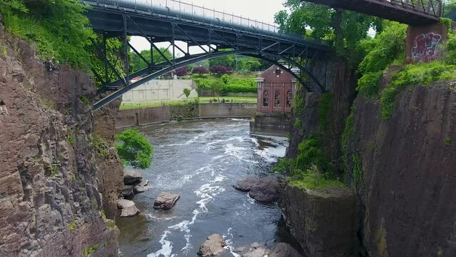A spectacular 4K drone shot of the historic Paterson Great Falls, located in Paterson, New Jersey. The camera moves forward over the waterfall and under a walking bridge crossing the Passaic River.