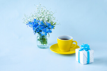 プレゼントとデルフィニウムとカスミソウのアレンジメントとコーヒー（水色の背景）