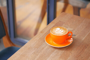 Hot latte coffee in orange color cup on wooden table 