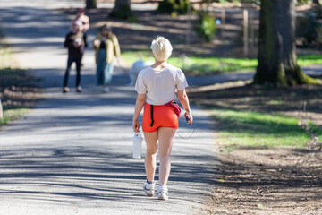 Young fit woman walking and running, working out, listening to music, in a park during warm sunny...