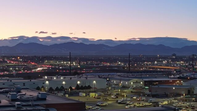 Clouds gather around Rocky Mountainson horizon at dusk as cars commute home passing industrial district