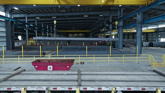 Aerial dolly above empty flatbed semi truck entering into steel pipe beam warehouse