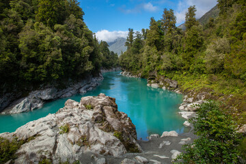 Brilliant turquoise water caused by glacial flour flows through Hokitika Gorge, surrounded by rocky limestone cliffs and lush vegetation on the South Island of New Zealand
