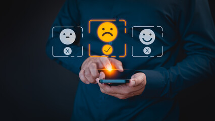 Engaging in an online customer feedback survey, a user utilizes their mobile phone to display an angry emoticon on a virtual screen, sharing their opinion and reviewing service satisfaction. - 769311834