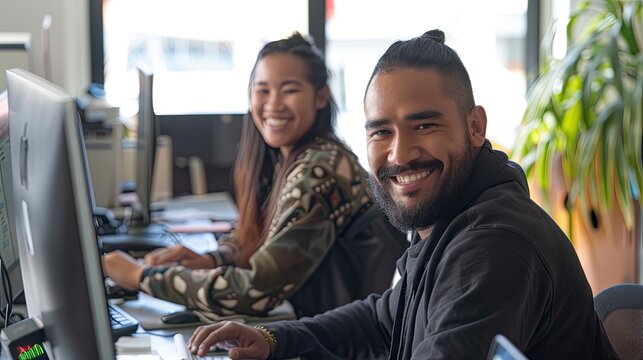 2 people working on a Website in an office setting smiling at the camera, one is MÄori. This image will represent Wordpress Support 