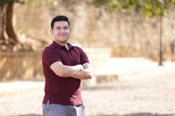 portrait of young mexican man with crossed arms wearing casual wine colored clothes looking at the...