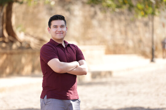portrait of young mexican man with crossed arms wearing casual wine colored clothes looking at the camera and smiling