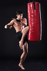 Man, fighter and boxing bag with kick in studio for self defence workout, martial arts or black...