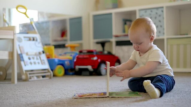 red hair little boy is sitting on the floor in the children's room and is pointing to the gate book, one year old