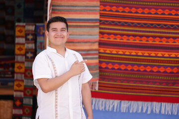 Portrait of young mexican man smiling in typical mexican clothing, looking at the camera pointing...