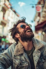 A man with a beard and sunglasses is smiling and wearing a denim jacket