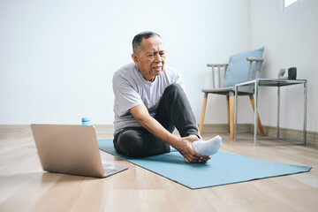 
Elderly Asian man touching his feet suffering from pain when exercising at home. Podiatry concept