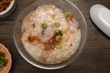 Asian thick rice porridge bubur chicken beef meat fish prawn rustic silver pot ladle serving in glass bowl fried shallots green onion chilli oil condiment