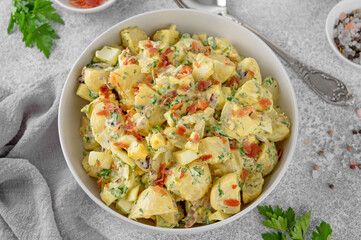 Fototapeta na wymiar Salad of potatoes, eggs, bacon and fresh herbs with mayonnaise and yogurt dressing in a bowl on a gray concrete background.