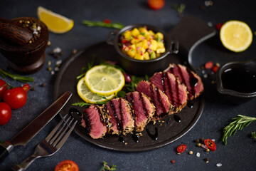 Sliced Organic grilled Tuna fillet covered with sesame seeds and mango salsa on black ceramic serving board