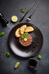 Tuna and avocado tartare with sesame seeds, capers and egg yolk on a dark ceramic plate with baguette bread crouton chips