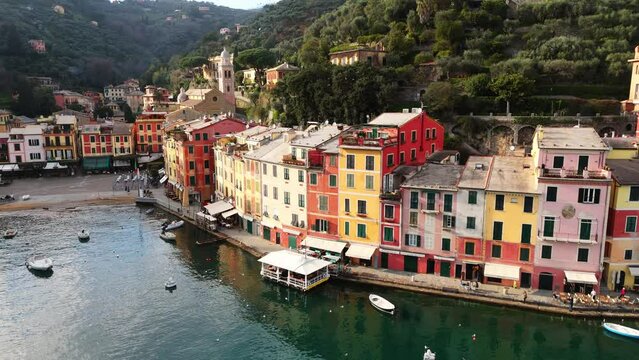 Colorful houses line the harbor of Portofino, Italy, with boats docked in calm waters at sunset, aerial view