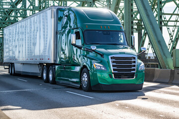 Green powerful big rig semi truck transporting cargo in dry van semi trailer running on the arched truss bridge