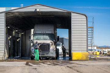 Washers wash a big rig semi truck with trailer at an industrial wash for large vehicles