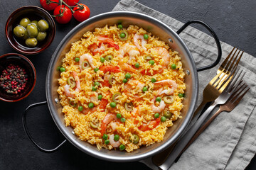 Traditional spanish seafood paella with rice, shrimps, olives and green peas in paellera on the table. Top view