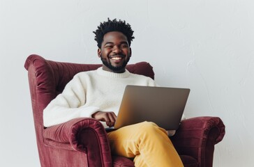 Smiling african american man sitting on bugundy design chair with portable laptop on knees over white background with copy space. - obrazy, fototapety, plakaty