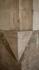 A corner of a building with a triangle shaped stone. The stone is missing and the wall is crumbling