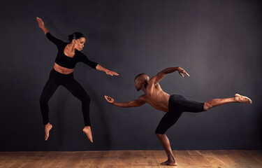 Dancers, dramatic and performance in studio with dark background, male and female ballerina being creative together. Athletics, competitive and sports for fitness, diverse people, art and movement. - Powered by Adobe
