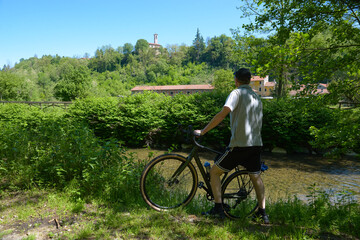 Bicycle ride in the greenery along the course of a river. Cycle pedestrian path along the Olona river near Lonate Ceppino town, Italy with the church of San Pietro Apostolo, 12th century