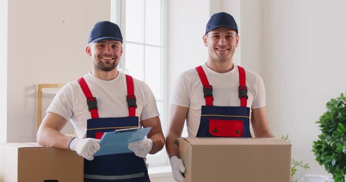 Portrait of two smiling men, movers from relocation service staff, holding box in hands, during office or home moving. Professional and friendly attitude ensures relocation process.