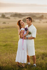 A couple in love in white clothes in a field at a sunset
