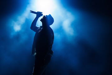 Silhouette of a Passionate Male Singer on Stage, Spotlight Shining During a Live Music Performance,...