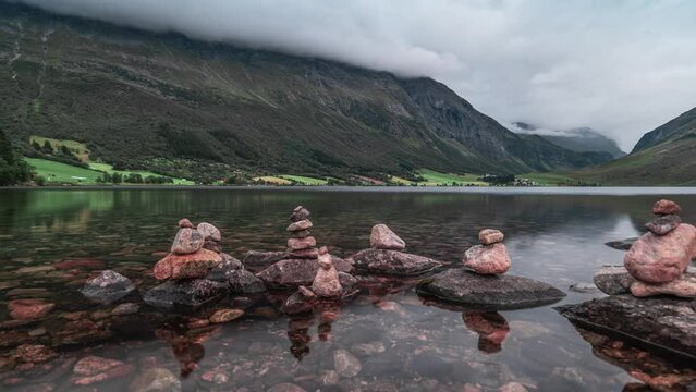 Stone cairns are arranged on the bank of the shallow lake surrounded by forest-covered mountains.