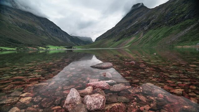 Forest-covered mountains are reflected in the still mirrorlike water of the shallow lake.