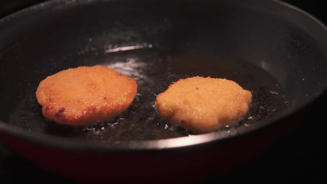 Flipping pork loin patties with green pepper and bechamel sauce in batter frying in a pan.
