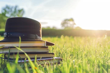 Foto op Canvas hat beside stack of books in sunny grassland © primopiano