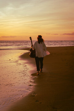Woman musician with guitar on the beach at sunset. Bali
