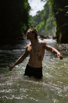 Young tattooed man at tropical waterfall, Bali island.