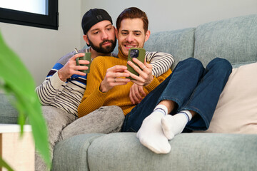 Homosexual couple lying on the sofa and using the phone together.