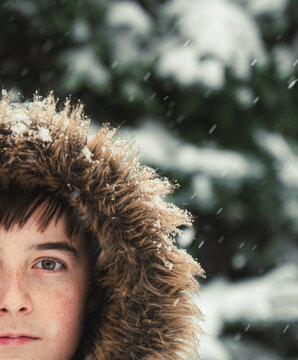Close up of boy wearing furry hood outside in snow on winter day.