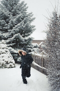 Happy boy wearing coat with furry hood outside in snow on winter day.