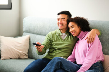 Multiethnic couple smile and watch TV, movie or film together on sofa.