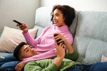 Multiethnic couple watching TV and using the phone together on sofa.
