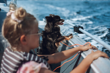 A girl and a dog enjoying a boat ride on a glorious summer day, both holding the rail and looking...