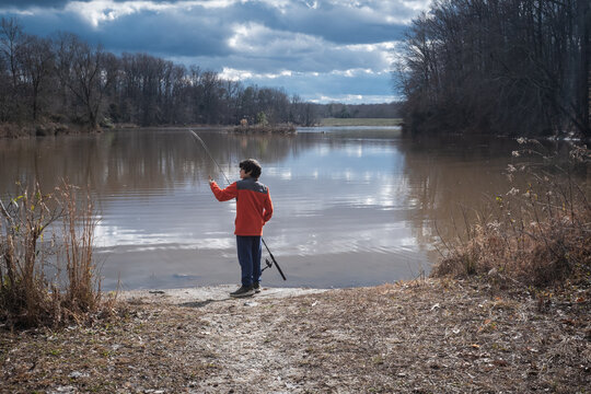 Young boy fishing from shore of lake in winter.
