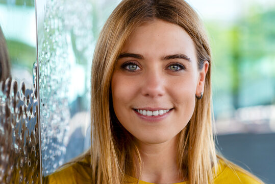 young woman's captivating gaze with a warm smile, wearing a yellow top