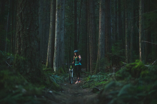 Woman standing next to her mountain bike on trail in the forest