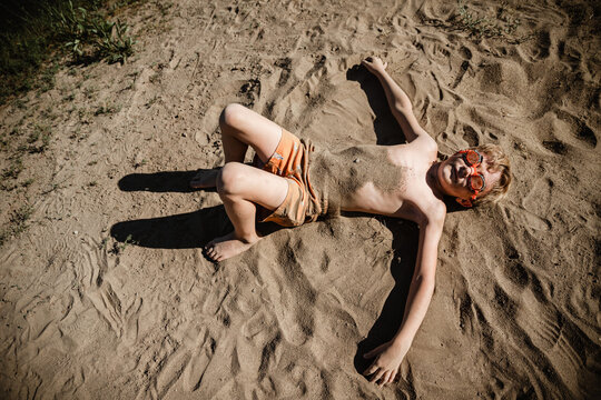 Young boy laying on beach covered in sand on summer day