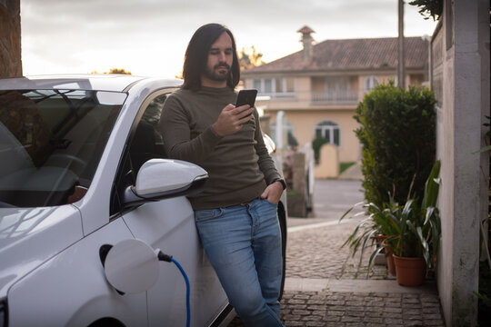 A man is charging an electric car parked in the house area.