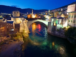 Tuinposter Stari Most Night view of the Old Bridge in Mostar city in Bosnia and Herzegovina. Neretva river. Unesco World Heritage Site. People walking over the bridge.